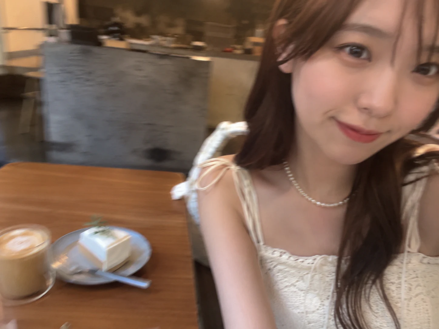 木のテーブル上のカフェオレとケーキを左側に置き、人物の顔を右へ寄せた横向き自撮りのAI生成例