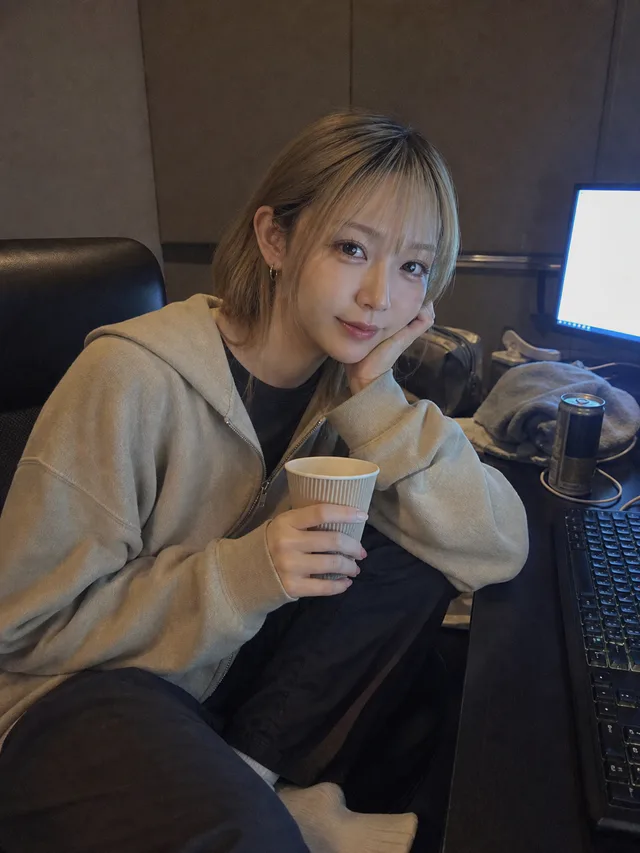 深夜のネットカフェ個室で、ベージュのパーカーを着た成人女性が紙コップを持って頬杖をつくAI生成のタイマー写真