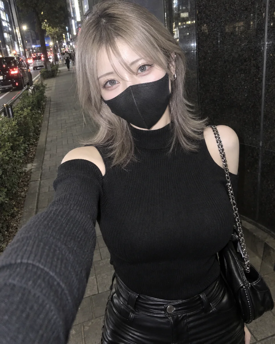 夜の街で、アッシュベージュのウルフヘアと黒マスク、肩開きニット、レザーパンツ姿の女性が自撮りしている