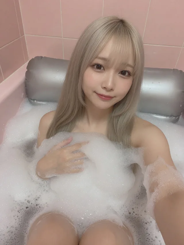 泡を手で寄せて微笑むプラチナブロンドの藤崎エマ。銀マットとピンクの浴室