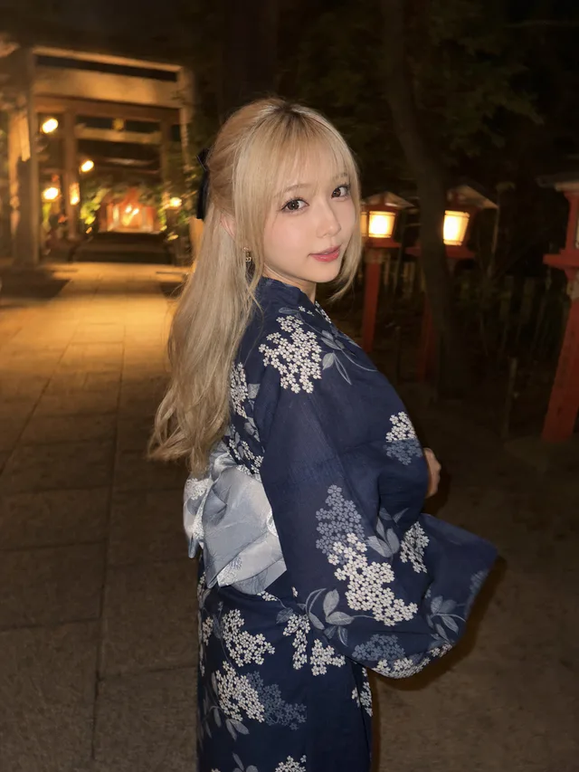夜の神社参道で、紺色の紫陽花柄浴衣を着たプラチナブロンドの成人女性がスマホフラッシュに振り返るAI生成写真