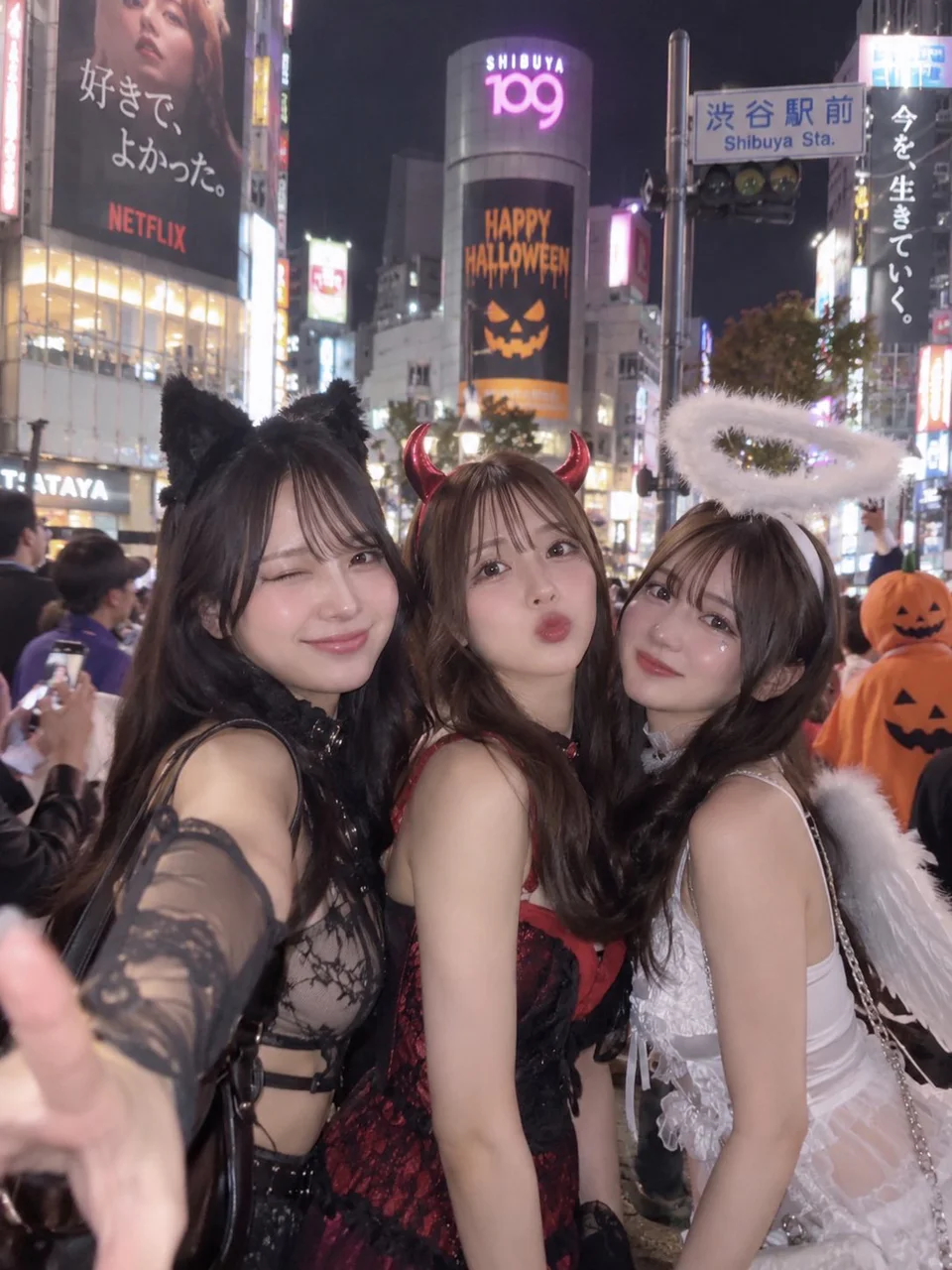 猫耳の黒い衣装、赤い悪魔衣装、白い天使衣装の3人の成人女性が、夜の渋谷で身を寄せて自撮りするAI生成画像