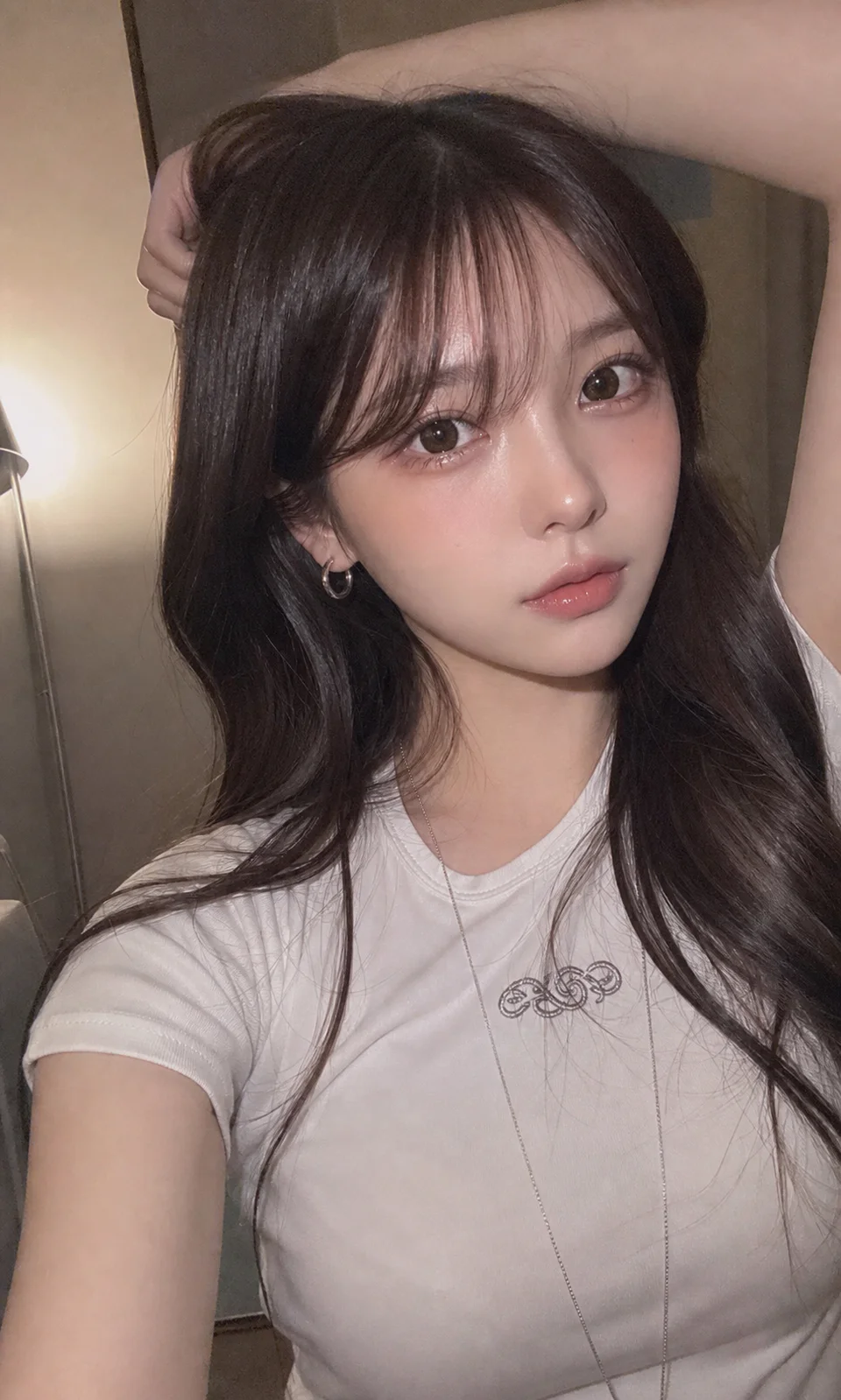 夜の室内で、白いTシャツを着た成人の日本人女性が片腕を頭上に上げ、スマートフォンで自然なセルフィーを撮っているAI生成画像