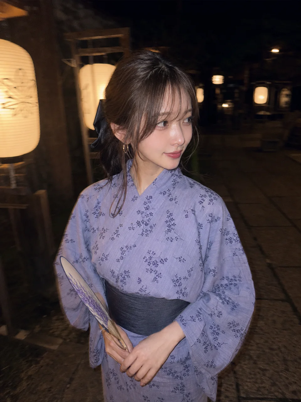 夜の神社境内で、淡いラベンダー色の花柄浴衣を着て団扇を持つ成人女性をスマホフラッシュで撮影したAI生成写真