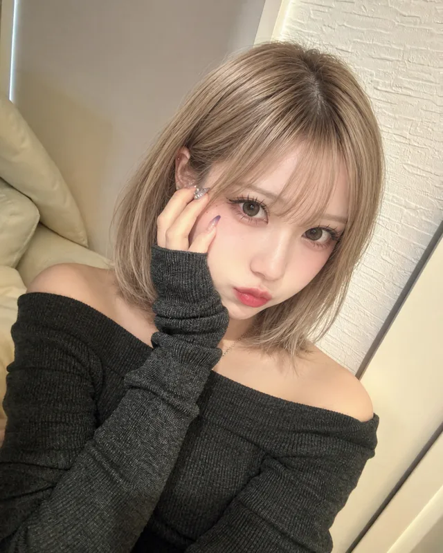 黒いオフショルダーニットの白瀬みるが、淡い色のソファで頬に片手を添えて写る近距離のセルフィー。