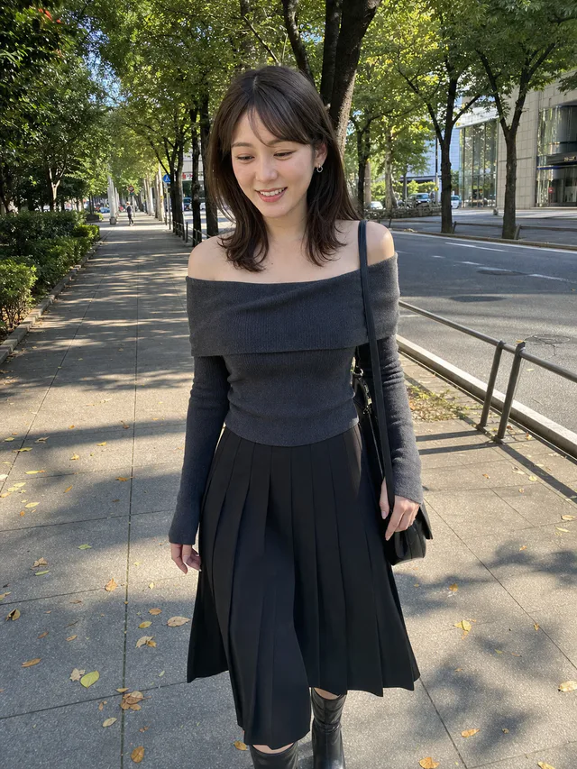 木漏れ日が差す街路樹沿いで、チャコールのニットと黒いスカートを着た成人女性が歩くAI生成のスマホ写真風ポートレート
